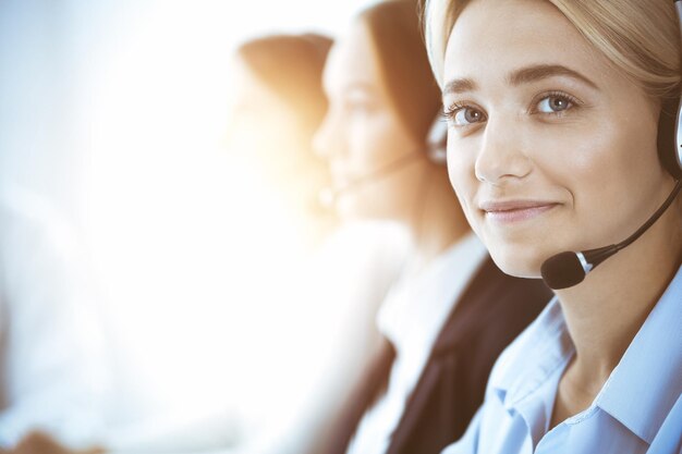 Concept de centre d'appels et de gens d'affaires. Belle femme d'affaires avec des écouteurs consultant les clients. Groupe de divers opérateurs téléphoniques au travail au bureau.