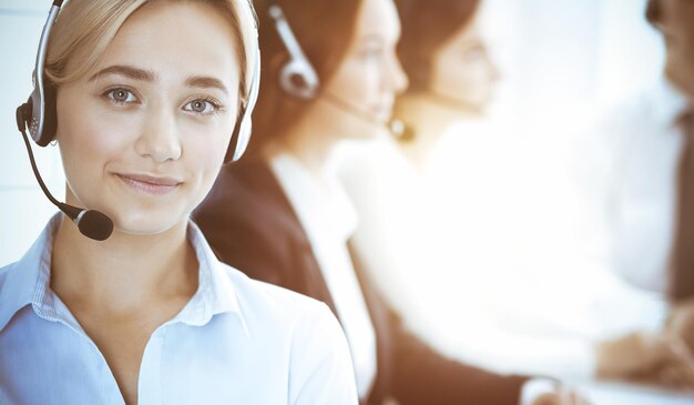 Concept de centre d'appels et de gens d'affaires. Belle femme d'affaires avec des écouteurs consultant les clients. Groupe de divers opérateurs téléphoniques au travail au bureau.