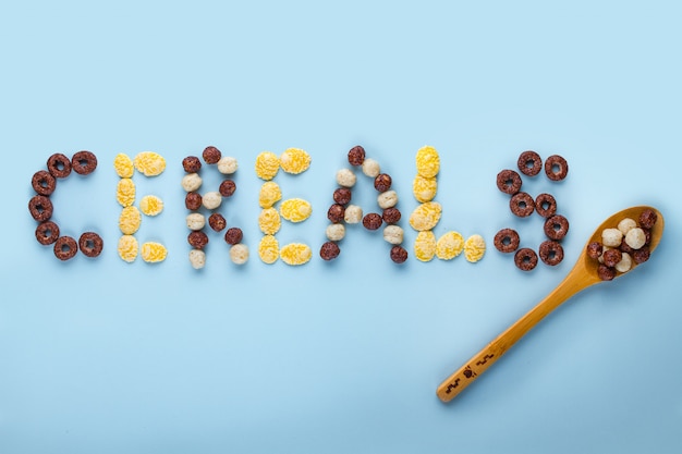 Concept de céréales. Cuillère avec boules de chocolat glacées, bagues et flocons de maïs pour un petit-déjeuner sec et sain sur une surface bleue