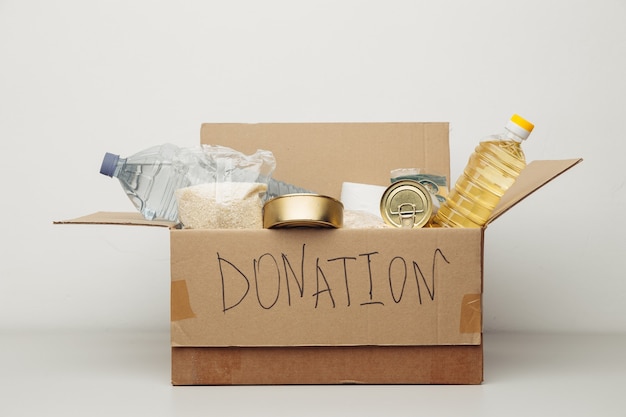 Concept de charité. Boîte en carton de don ouvert avec divers aliments sur un mur blanc