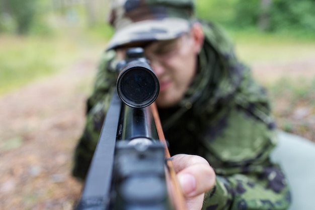 concept de chasse, de guerre, d'armée et de personnes - gros plan d'un jeune soldat, d'un garde forestier ou d'un chasseur avec une arme à feu dans la forêt