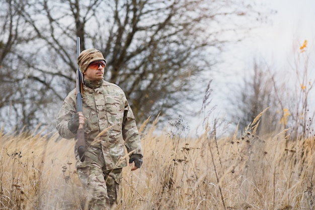 Concept de chasse, guerre, armée et personnes - jeune soldat, ranger ou chasseur avec arme à feu marchant dans la forêt