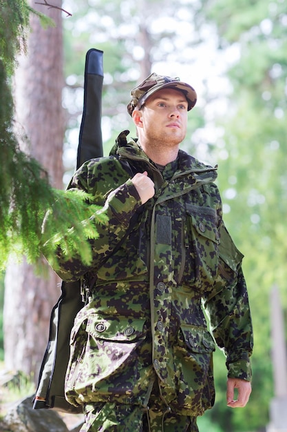 Concept de chasse, guerre, armée et personnes - jeune soldat, ranger ou chasseur avec arme à feu marchant dans la forêt