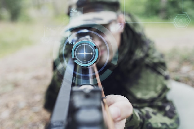 concept de chasse, de guerre, d'armée, de technologie et de personnes - gros plan d'un jeune soldat ou d'un tireur d'élite tenant une arme à feu avec projection d'écran virtuel et visant dans la forêt