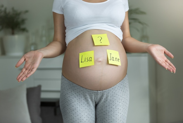 Concept de choisir le nom du bébé. Jeune femme régnant avec des noms écrits sur le ventre