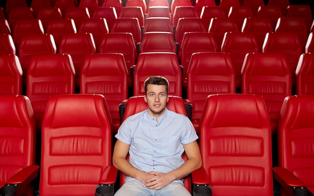 concept de cinéma, de divertissement et de personnes - jeune homme heureux regardant un film seul dans un auditorium de théâtre vide