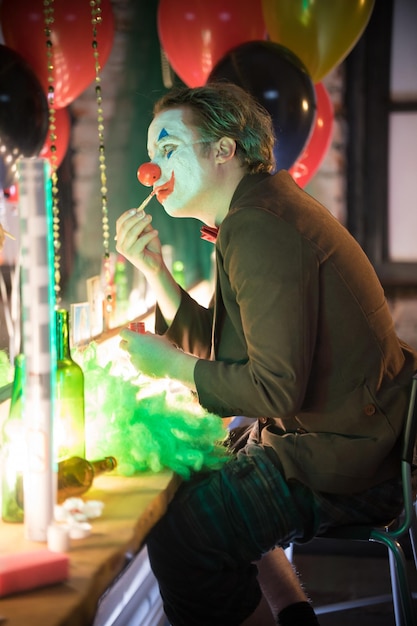 Concept de clown un homme clown assis dans le vestiaire et peignant un sourire rouge sur son visage