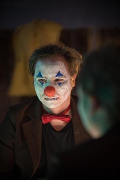 Concept de clown un homme avec un visage peint de clown fissuré regardant dans le miroir