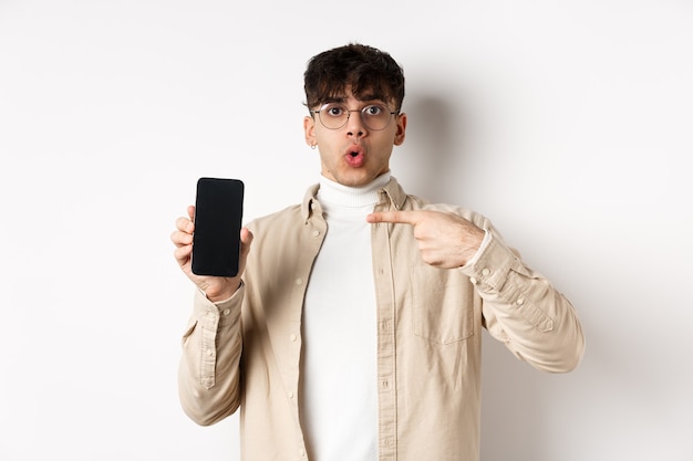 Concept de commerce électronique. Portrait de jeune homme pointant sur l'écran du téléphone mobile