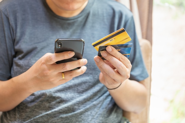 Concept commercial, financier, de paiement et de technologie. Homme asiatique tenant deux fausses cartes de crédit de maquette et utilisant un smartphone mobile.