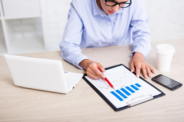 Concept commercial et statistique - femme d'affaires assise dans un bureau moderne avec des tableaux et des graphiques