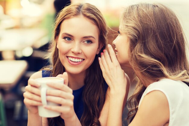 concept de communication et d'amitié entre les gens - jeunes femmes souriantes buvant du café ou du thé et bavardant au café en plein air