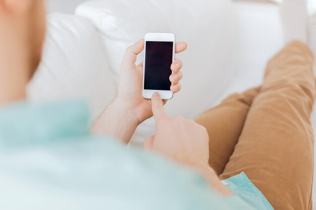 concept de communication, d'entreprise, de maison et de technologie - gros plan d'un homme avec un message texte sur smartphone assis sur un canapé à la maison