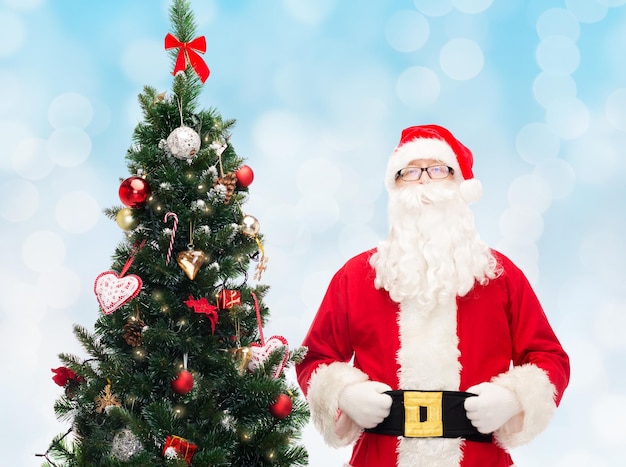 concept de concept de vacances et de personnes - homme en costume de père noël avec arbre de noël sur fond de lumières bleues