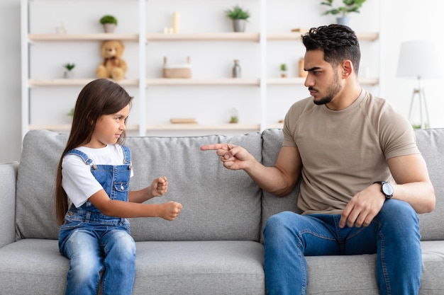 Concept de conflits familiaux. Un père fou en colère grondant sa fille triste pour un mauvais comportement à la maison, un père parent sérieux punit une fille désobéissante qui pointe le doigt et exige de la discipline.