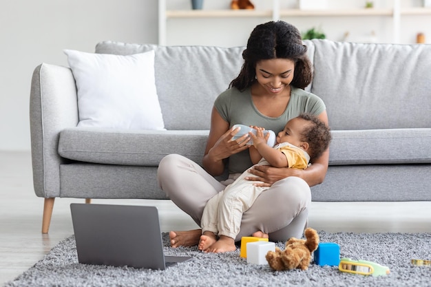 Concept de congé de maternité jeune mère noire donnant une bouteille avec de l'eau à bébé