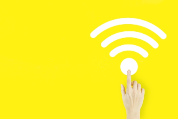 Concept de connexion réseau d'entreprise. Doigt de la main de la jeune femme pointant avec l'hologramme Wi-Fi sur fond jaune. Concept sans fil Wi-Fi.