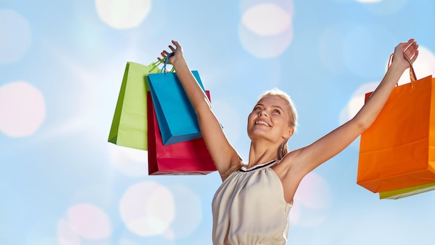 concept de consommation, de vente et de personnes - femme souriante avec sac à provisions levant les mains sur fond de lumières bleues