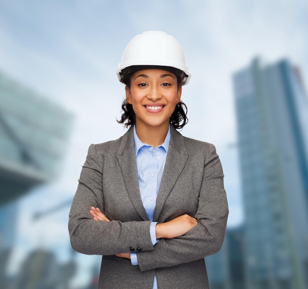 concept de construction, de développement, de construction et d'architecture - femme d'affaires souriante en casque blanc avec les bras croisés