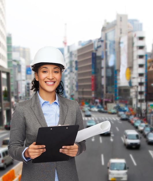 concept de construction, de développement, de construction et d'architecture - femme d'affaires souriante en casque blanc avec presse-papiers et plan