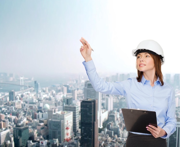 concept de construction, de développement, de construction et d'architecture - femme d'affaires souriante en casque blanc avec presse-papiers pointant du doigt