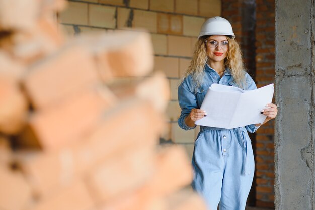 Concept de construction. Jolie femme constructeur en salopette et casque travaillant sur le chantier de construction.