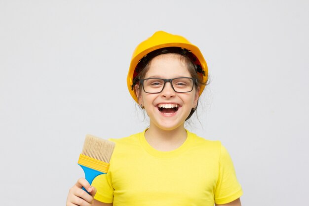Concept de construction et de personnes - petite fille souriante dans un casque de protection et des lunettes avec un pinceau