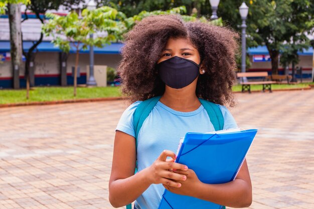 Concept De Coronavirus Covid-19. écolière Portant Un Masque Médical Pour La Protection De La Santé Contre Le Virus De La Grippe. Fille étudiante Avec Sac à Dos Et Livres - Portrait En Plein Air. Enfant De Retour à L'école.