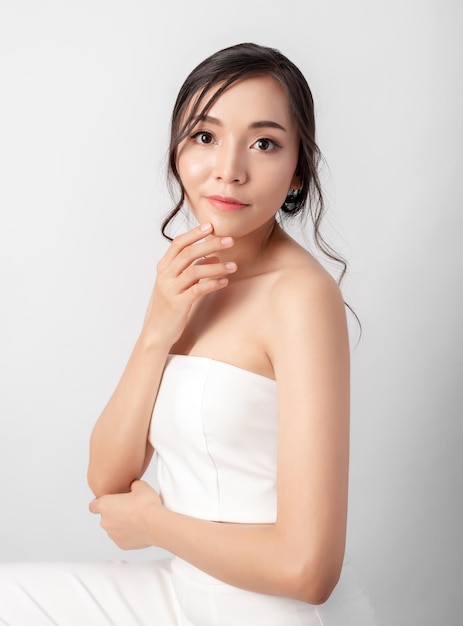 Concept cosmétique de beauté de jolie femme asiatique posant à la mode montrant la peau du visage et du corps portant une robe blanche sur fond blanc