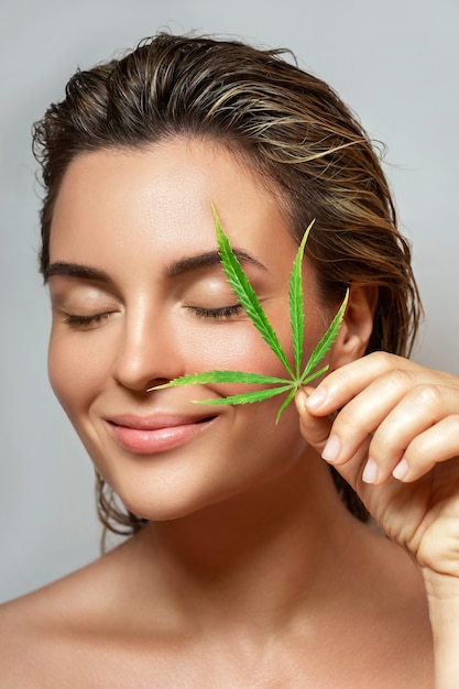 Concept de cosmétiques CBD. Belle femme avec une feuille de cannabis sur fond gris