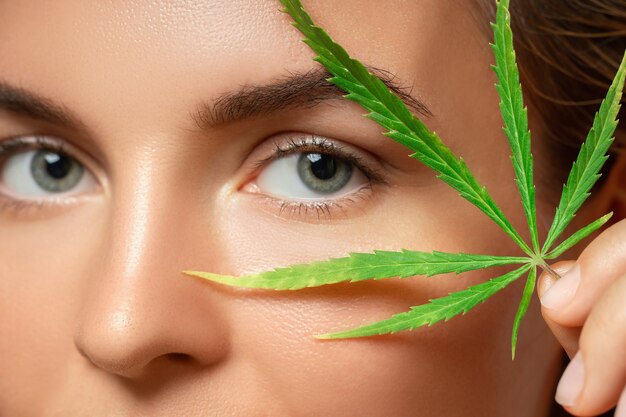 Concept de cosmétiques CBD. Belle femme avec une feuille de cannabis sur fond gris