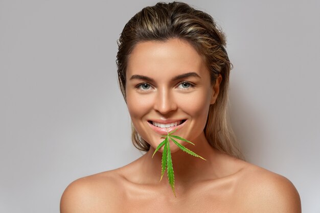 Concept de cosmétiques CBD. Belle femme avec une feuille de cannabis sur fond gris