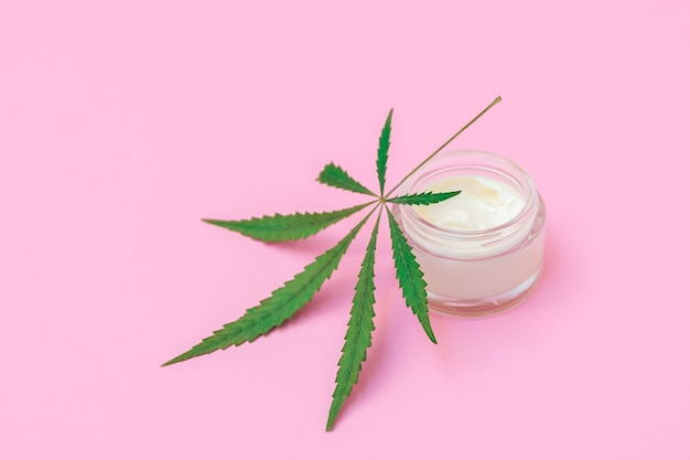 Concept de cosmétiques infusés au cannabis bouteille de crème avec feuille de chanvre sur fond rose tendre avec copie s...