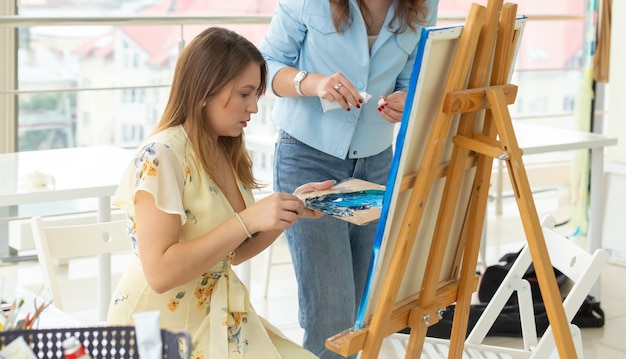 Concept de cours d'art, de dessin et de créativité - Gros plan sur une étudiante assise devant un chevalet avec palette et pinceau. Le professeur l'aide