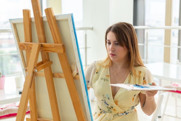 Concept de cours d'art, de dessin et de créativité - Étudiante assise devant un chevalet avec palette et pinceau