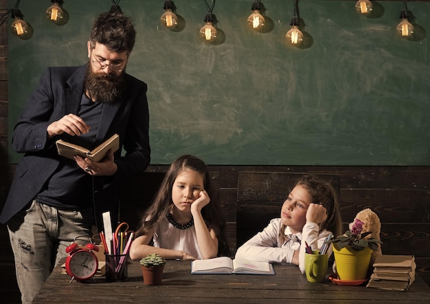 Concept de cours ennuyeux Homme avec barbe enseigne aux écolières lire un livre Enfants ennuyés et fatigués écoutant le professeur Enseignant et filles élèves dans le tableau de classe sur fond