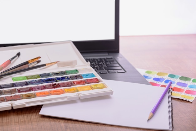 Concept de couverture de cours de dessin en ligne avec une feuille d'ordinateur portable de peintures et de pinceaux en papier sur un bureau en bois de ...