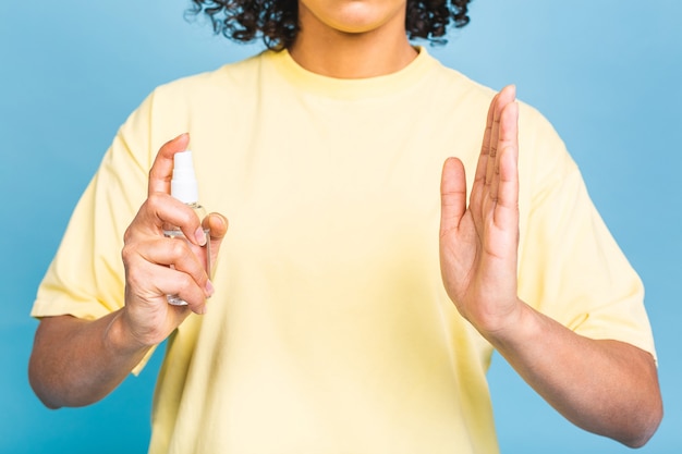 Photo concept covid-19. femme noire afro-américaine désinfectant la peau avec désinfectant pour les mains isolé sur fond bleu. concept de coronavirus.