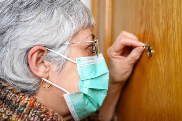 Concept Covid-19. Reste à la maison. Auto-isolement pour prévenir la pandémie de coronavirus. Haute femme en masque de protection vert regarde à travers le judas.