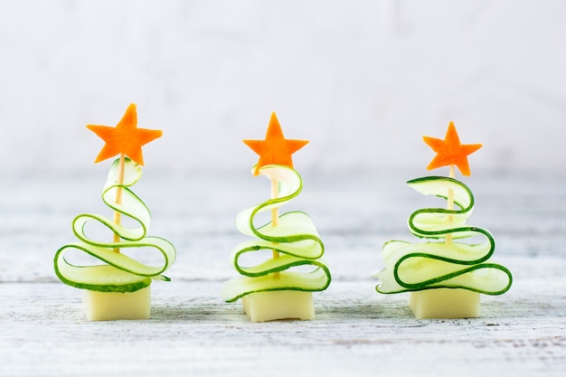 Concept créatif défini des arbres de Noël de concombre, de fromage et d'étoile de carotte. Nourriture pour enfants drôle pour la fête du nouvel an sur fond gris avec espace de copie