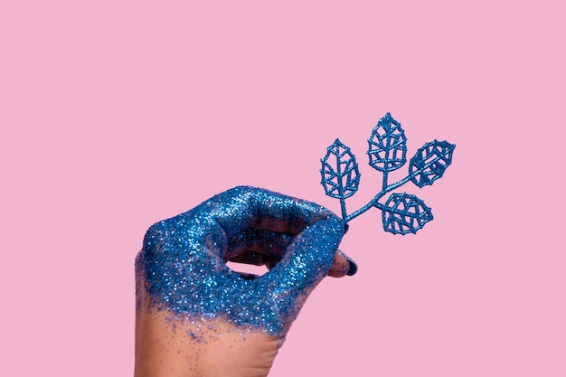 Concept créatif de Noël de main féminine avec des paillettes bleues et des brindilles scintillantes sur fond de couleur