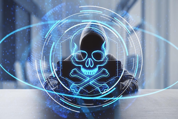 Concept créatif de piratage et de piratage en ligne avec une personne en sweat à capuche sans visage travaillant avec un ordinateur portable sur fond de bureau sombre et une double exposition d'hologramme numérique de crâne et d'os bleus