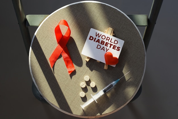 Photo concept créatif à plat de la journée mondiale du diabète avec des médicaments et une seringue pour le symbole du sang en ruban rouge