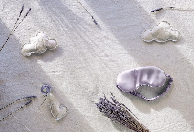Concept créatif de sommeil nocturne sain avec couleur lavande Fond textile ivoire blanc cassé Masque de sommeil en soie Peluches nuages et formes de coeur Fleurs de lavande sèches Ombres de lumière naturelle