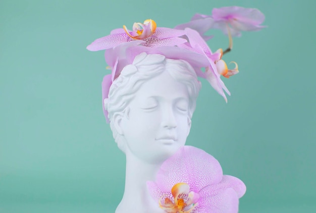 Concept créatif tête colorée d'une ancienne statue cheveux faits de fleurs fraîches Sculpture en plâtre du visage de la femme sur fond d'orchidée Concept surréaliste romantique de la vision de la mode printemps-été