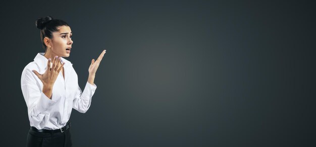 Photo concept de crise avec une jeune femme confuse avec des mains levées isolées sur fond gris foncé abstrait avec place pour votre logo ou maquette de texte