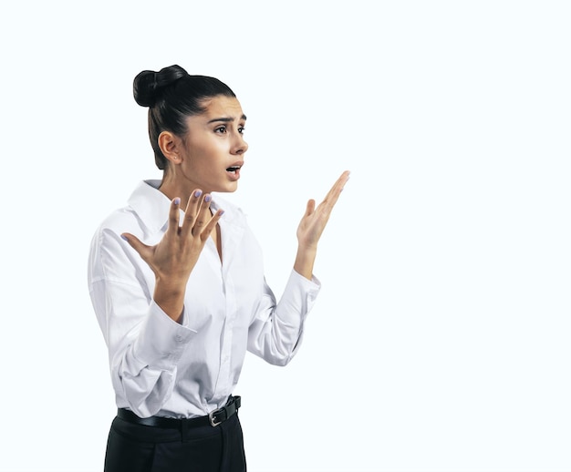 Concept de crise avec une jeune femme indignée en chemise blanche avec des mains levées isolées sur fond de mur clair gros plan