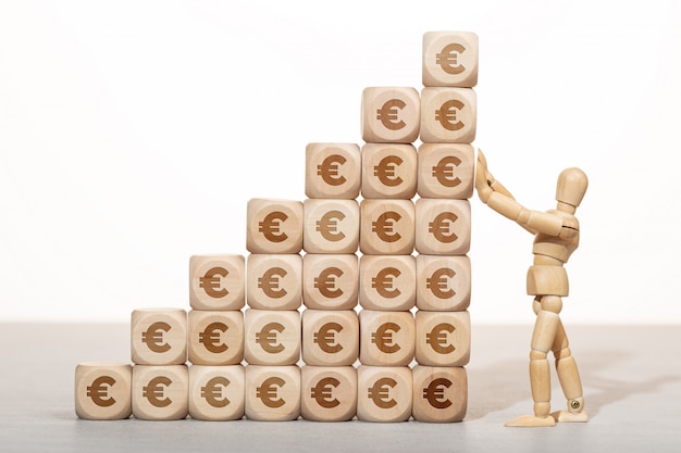 Concept de croissance, de richesse ou de richesse. Mannequin en bois tenant une pile de blocs en bois empilés avec le symbole de l'euro