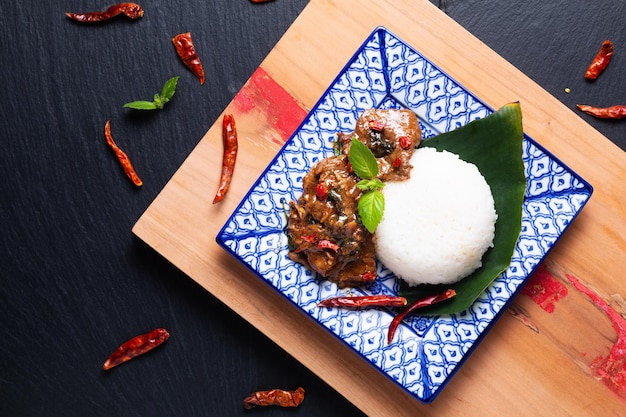 Concept de cuisine asiatique Sauté de boeuf au basilic sacré thaïlandais et riz au jasmin Khao Pad Pad Kra Pow Nua dans la tradition thaïlandaise assiette en céramique sur planche de bois et fond en pierre d'ardoise noire avec espace de copie