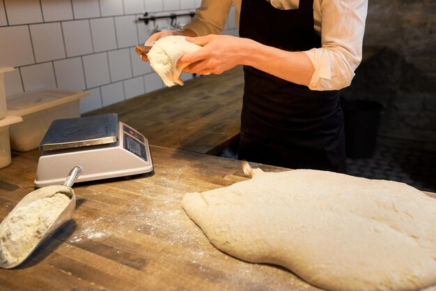 concept de cuisine, de boulangerie et de personnes - chef ou boulanger portionnant la pâte avec un coupe-banc à la boulangerie